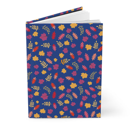 HARDCOVER JOURNAL, MATTE, RULED, 5X7, SEWN BIND, CLEAN-TEAR PAGES – FALL FOLIAGE, featuring a deep-blue cover adorned with vibrant autumn leaves, standing upright with pages fanned slightly open.