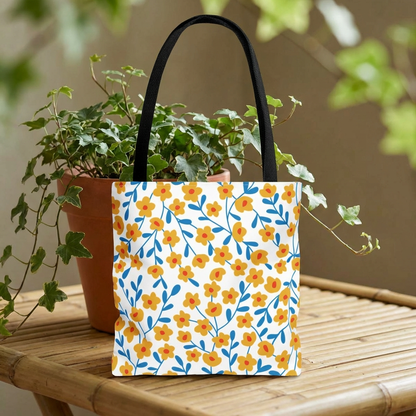 Buttercup Cream Tote Bag on wooden surface, featuring small yellow-orange flowers with blue stems. Black handles complement its cheerful design, ideal for summer outings, reflecting FireBrook Essentials’ uplifting style.