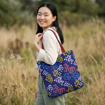 Midnight Garden Tote Bag over shoulder, featuring a navy base with vibrant floral clusters. A young woman wears the bag, highlighting its roomy, stylish design ideal for everyday joy and convenience.