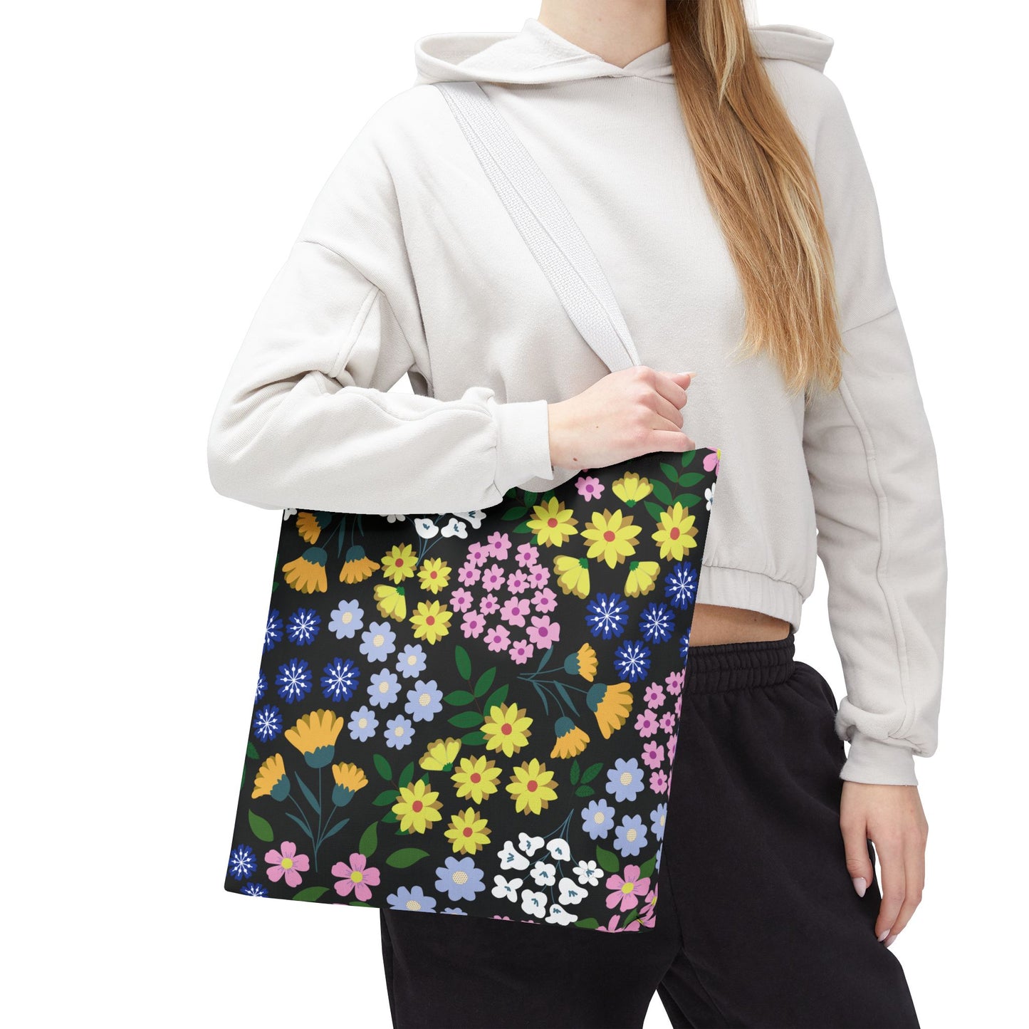 Person wearing a light-colored hoodie carries the Floral Tote Bag, featuring colorful flowers on a black background, perfect for summer outings. Ideal for brightening your day with cheerful, stylish design.