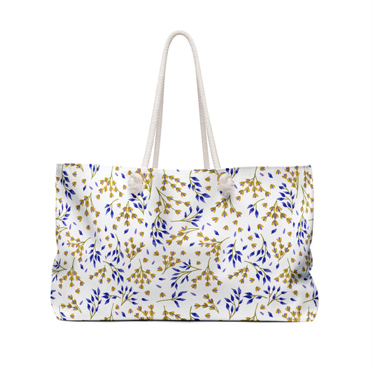 Weekender Bag with thick white rope handles, featuring a white fabric adorned with gold and blue leafy sprigs, perfect for stylish travel, offering spacious storage and a luxurious cream interior.