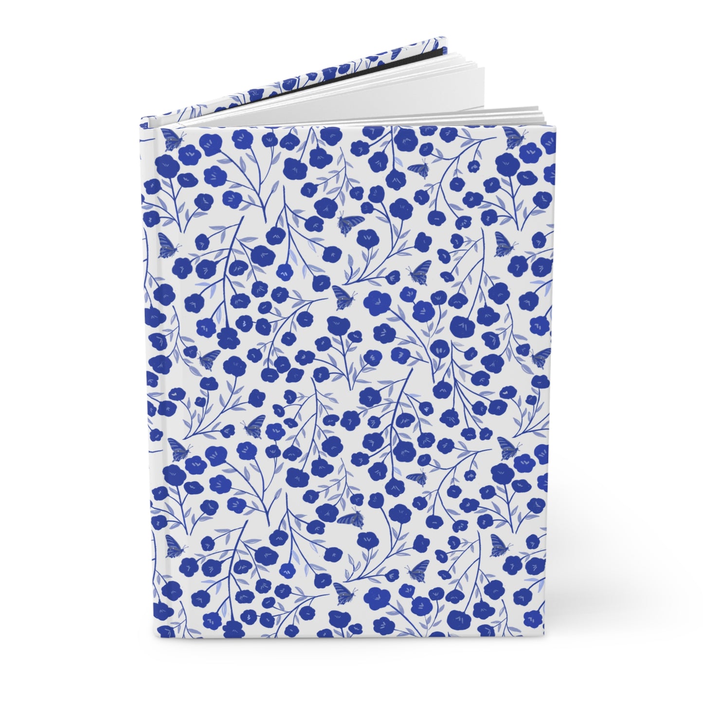 HARDCOVER JOURNAL, MATTE, RULED, 5X7, SEWN BIND, CLEAN-TEAR PAGES – INDIGO PETALS, with white cover featuring a blue floral and butterfly pattern, slightly fanned open to show durability and style.