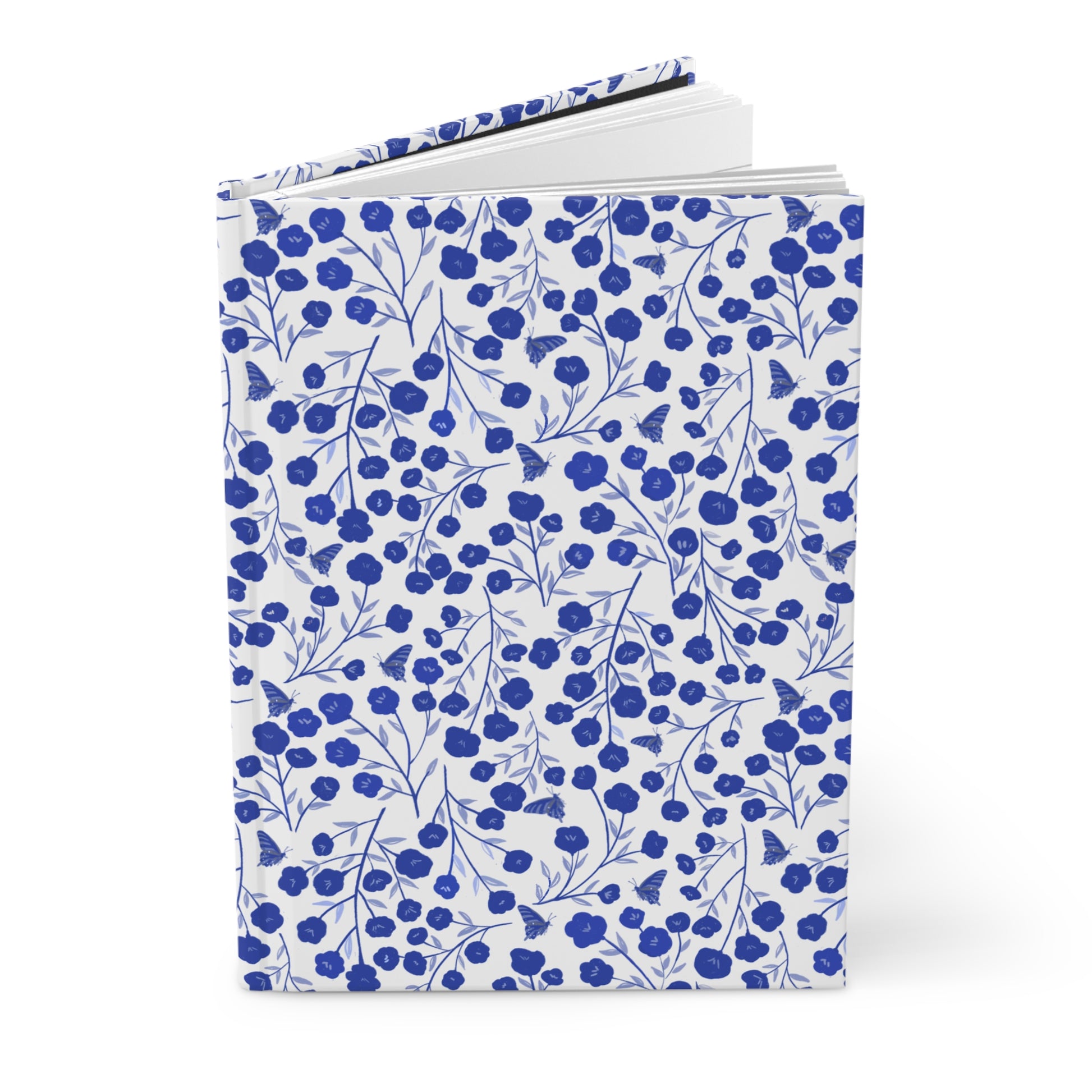 HARDCOVER JOURNAL, MATTE, RULED, 5X7, SEWN BIND, CLEAN-TEAR PAGES – INDIGO PETALS, with white cover featuring a blue floral and butterfly pattern, slightly fanned open to show durability and style.