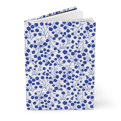 HARDCOVER JOURNAL, MATTE, RULED, 5X7, SEWN BIND, CLEAN-TEAR PAGES – INDIGO PETALS, with white cover featuring a blue floral and butterfly pattern, slightly fanned open to show durability and style.