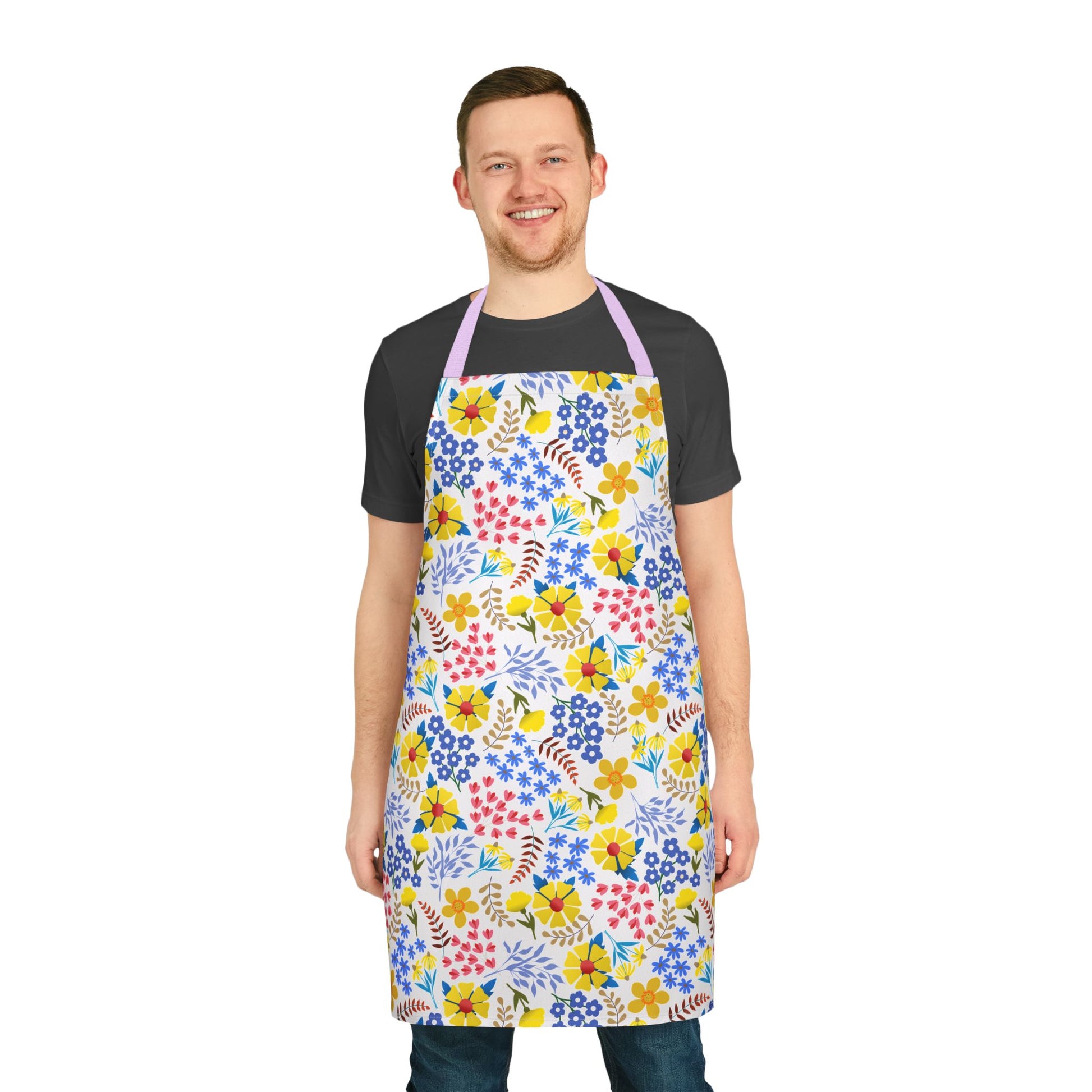 Smiling man wearing the Apron Floral Design from FireBrook Essentials, showcasing vibrant multicolored floral patterns on a white base with light purple straps, perfect for stylish cooking and crafting.