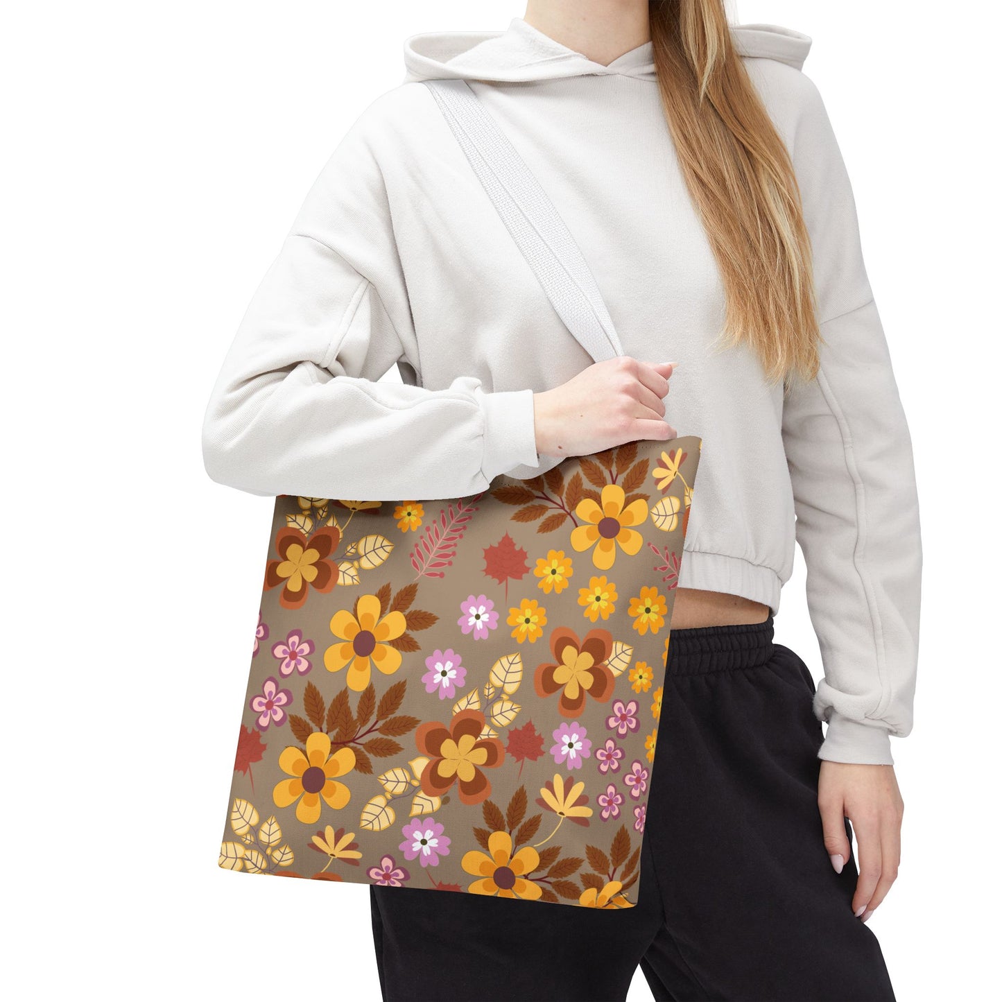 The Harvest Brown Bloom Tote Bag, with its retro-style autumnal floral pattern, complements a light-beige hoodie and black pants. Ideal for joyful outings, embodying FireBrook Essentials' blend of style and positivity.