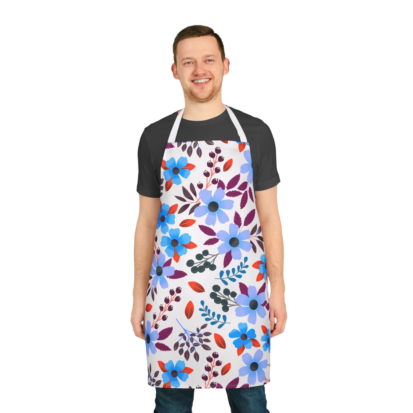 Smiling young man in a black t-shirt and jeans models the FireBrook Designs Floral Apron, featuring vibrant blue, purple, and red flowers. Ideal for cooking and hosting, emphasizing comfort and style.