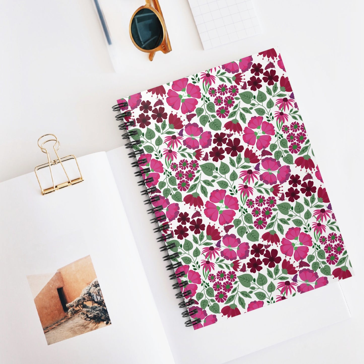 Floral Spiral Notebook with vibrant pink and burgundy flowers, surrounded by an open magazine and sunglasses, embodies FireBrook Designs' joyful, stylish approach to practical and creative essentials.