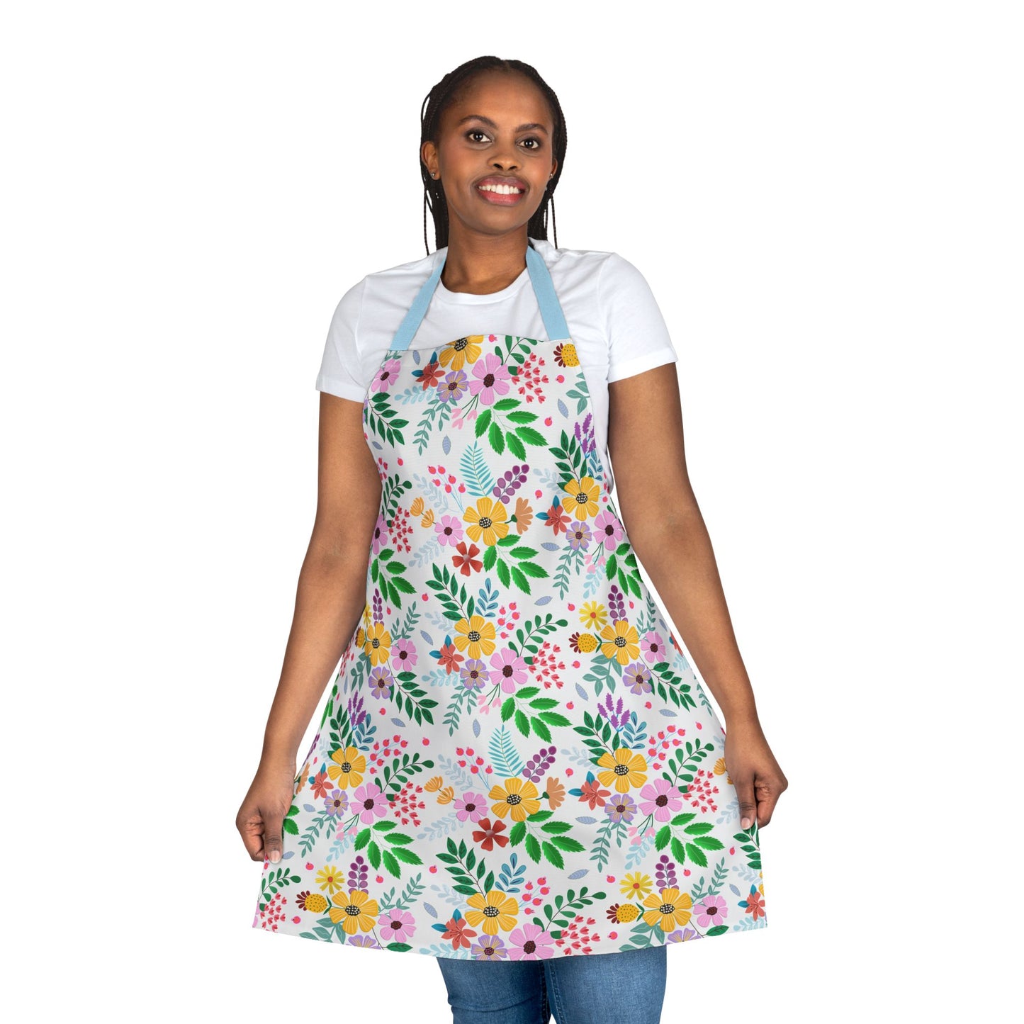 Woman wearing a Floral Apron with colorful spring flowers, over a white t-shirt and blue jeans, smiling and holding the apron sides. Perfect for baking and crafting, combining style and comfort.
