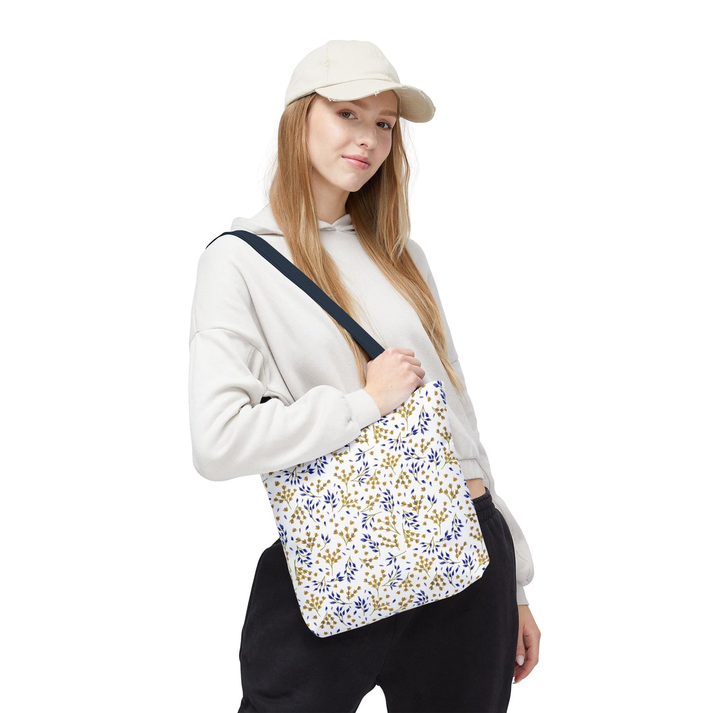 Young person wearing a light-colored hoodie and beige cap, carrying the Wild Herb Garden Tote Bag with a gold and blue botanical pattern, capturing FireBrook Designs' joyful and stylish essence.