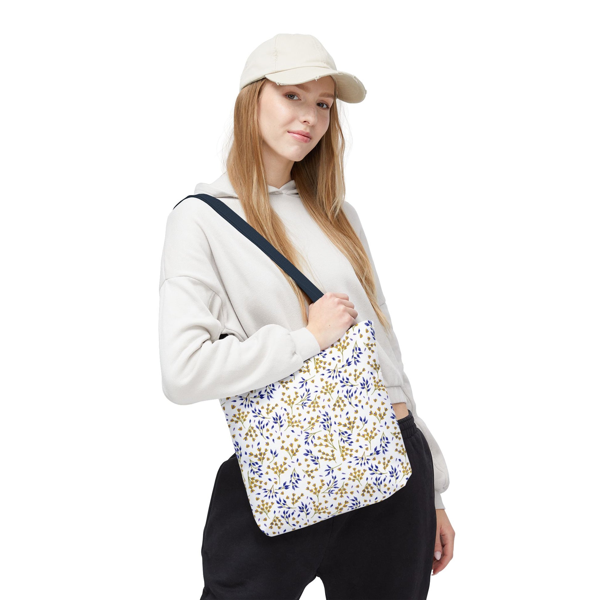 Young person wearing a light-colored hoodie and beige cap, carrying the Wild Herb Garden Tote Bag with a gold and blue botanical pattern, capturing FireBrook Designs' joyful and stylish essence.