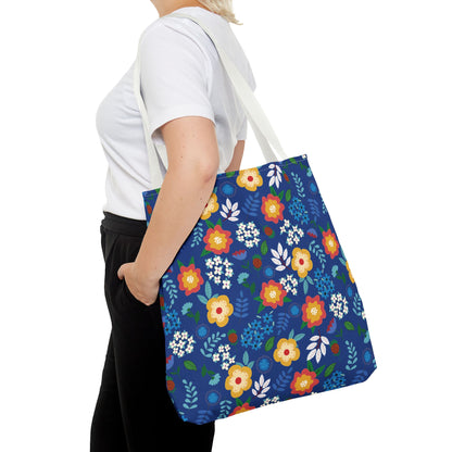 Person carrying a Cornflower Patch Tote Bag, decorated with vibrant stylized flowers. Ideal for summer outings, this durable polyester bag from FireBrook Designs embodies joyful, uplifting style with reinforced handles and ample space.