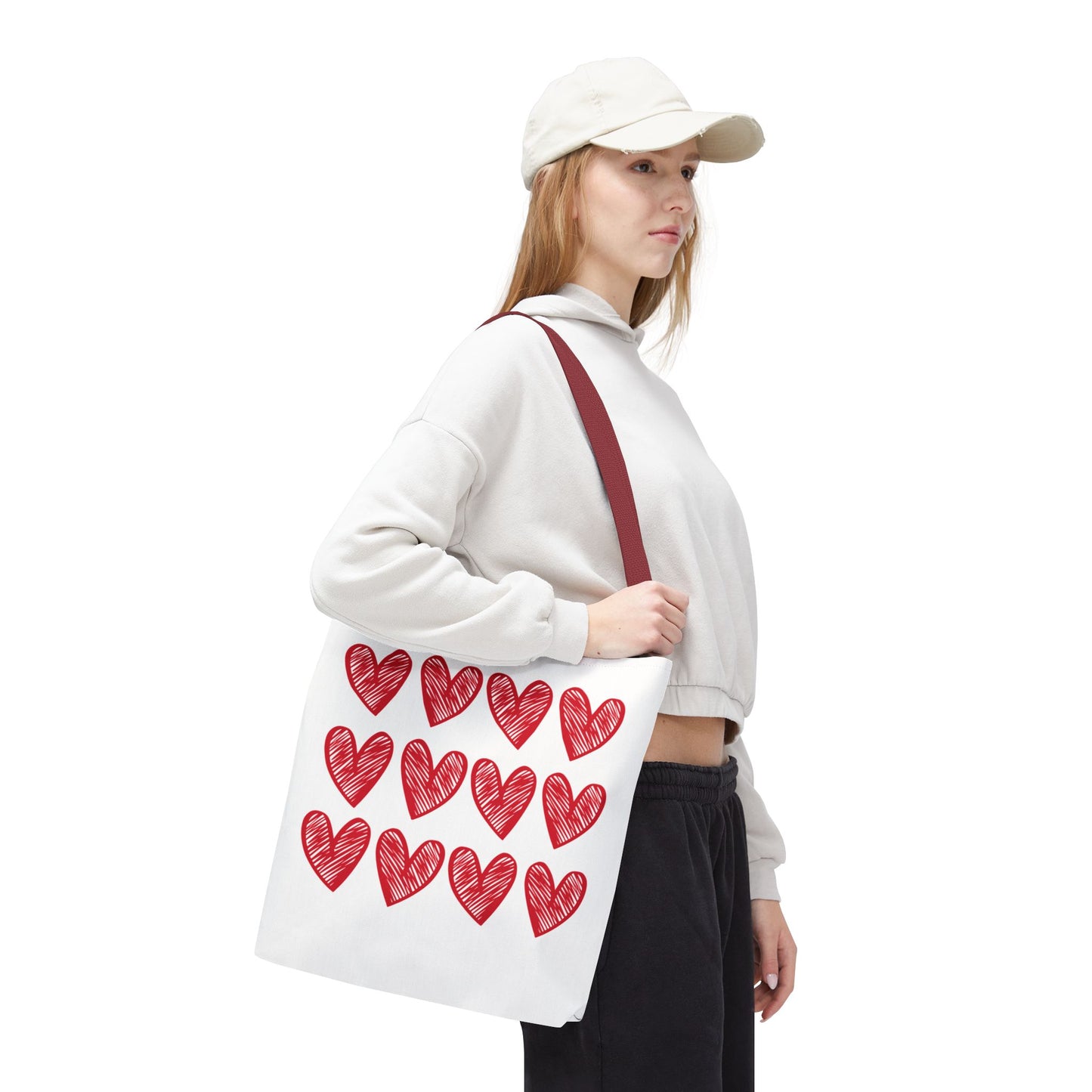Hearts Tote Bag showcasing a white fabric adorned with playful red heart patterns. The bag is held by a person, emphasizing its durability and spacious boxed corners, embodying FireBrook Designs' joyful and stylish ethos.