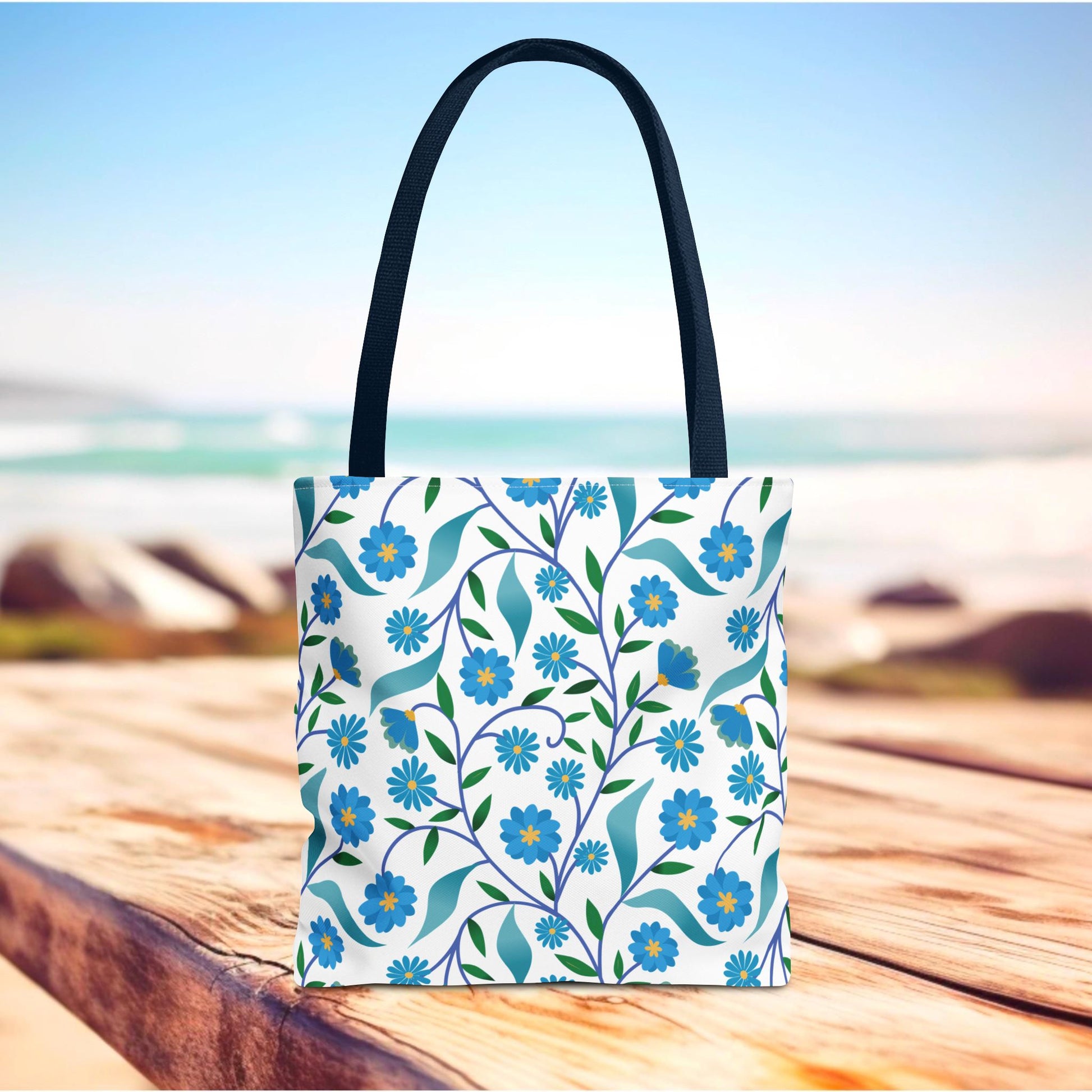 Blue Floral Tote Bag with dark handles, featuring vibrant blue flowers and green leaves on a white background, ideal for summer outings. Perfect blend of durability and cheerful design from FireBrook Designs.