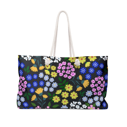 Weekender Bag with a vibrant floral print on black, featuring sturdy white rope shoulder straps. Ideal for stylish travel, it combines practicality and elegance, reflecting FireBrook Essentials' commitment to uplifting design.