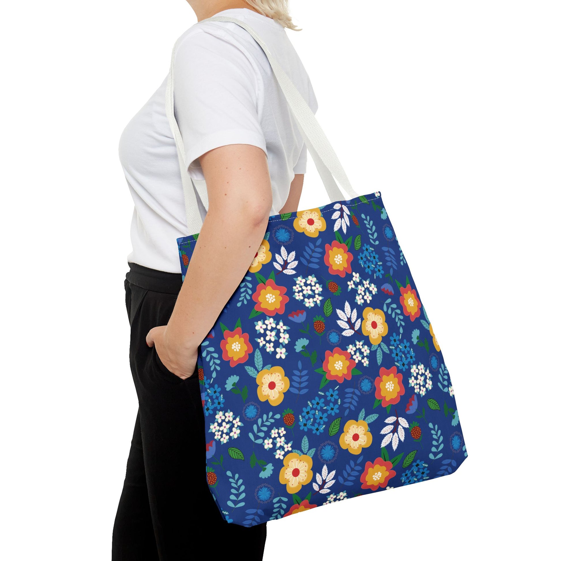 A person carries a Floral Tote Bag with a vibrant, multicolored floral pattern against a deep blue background, showcasing its cheerful and durable design, ideal for joyful summer outings.