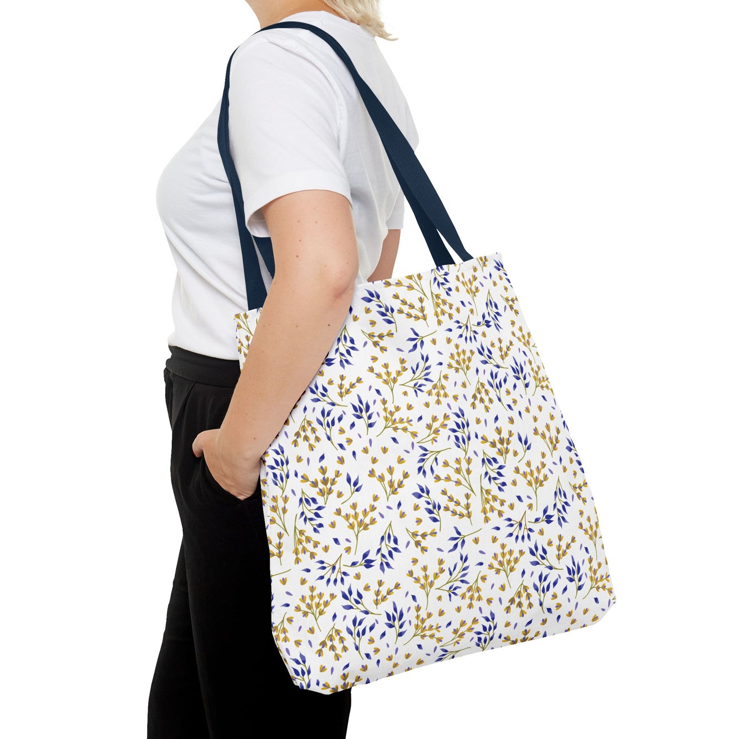 Person wearing plain attire carries the Wild Herb Garden Tote Bag, featuring a white base with blue-and-gold leaf pattern and navy straps, ideal for vibrant summer outings.
