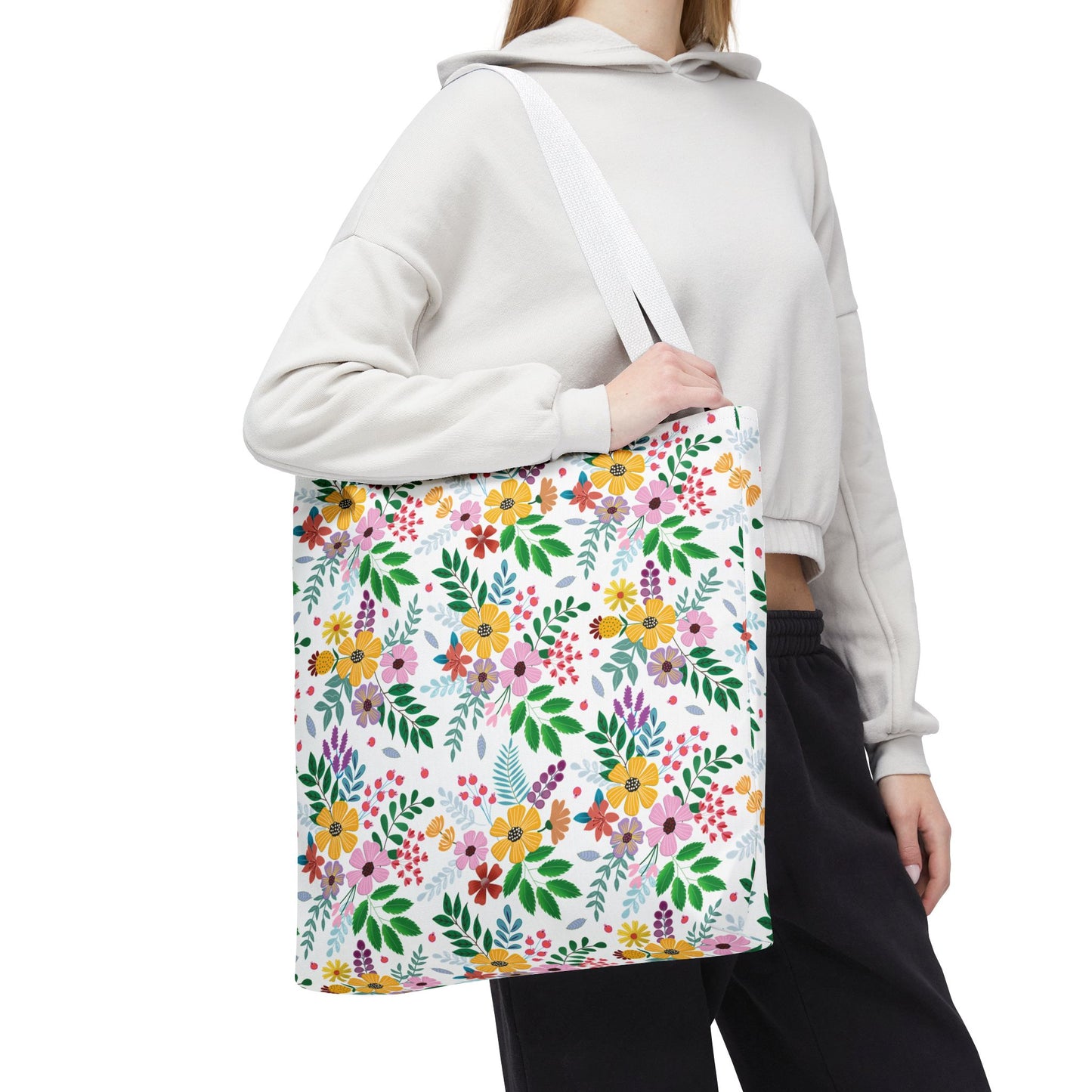 Person wearing a light-colored hoodie and black pants, carrying a Floral Tote Bag with multicolored flowers and green leaves, ideal for bright, joyful summer outings, designed by FireBrook Essentials.