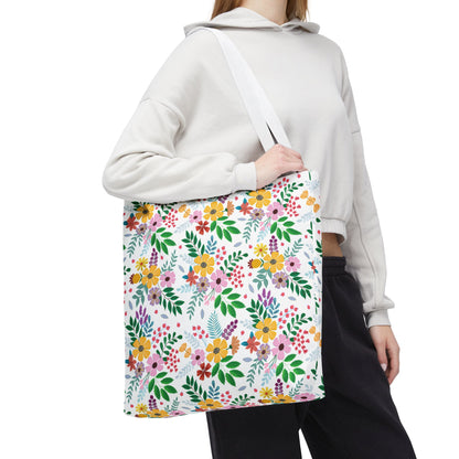 Person wearing a light-colored hoodie and black pants, carrying a Floral Tote Bag with multicolored flowers and green leaves, ideal for bright, joyful summer outings, designed by FireBrook Essentials.