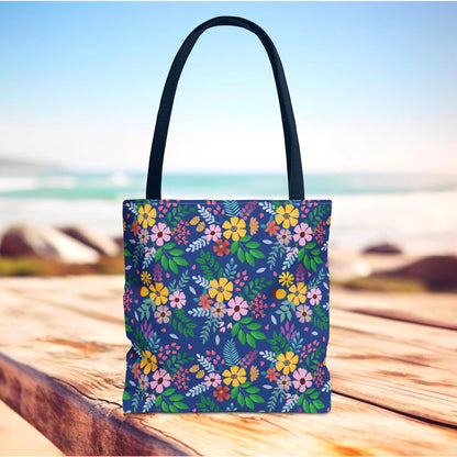Deep Sea Floral Patch Tote Bag with black handles, featuring a vibrant floral pattern on navy, ideal for summer outings or beach trips, displayed on a sunlit wood surface with ocean backdrop.