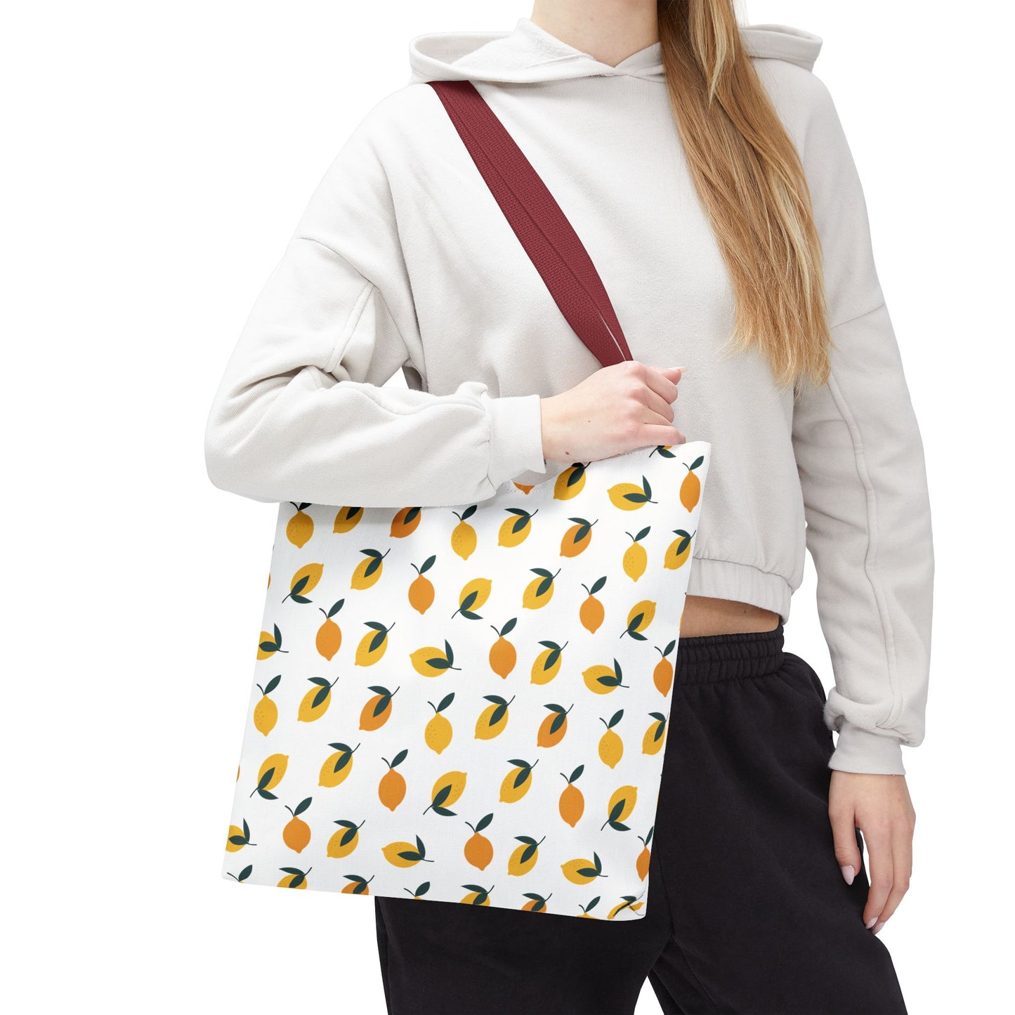 A person carries the Lemon Drop Toss Tote Bag, showcasing its burgundy-red strap and vibrant lemon pattern, embodying FireBrook Essentials' cheerful and stylish design ethos for joyful everyday use.