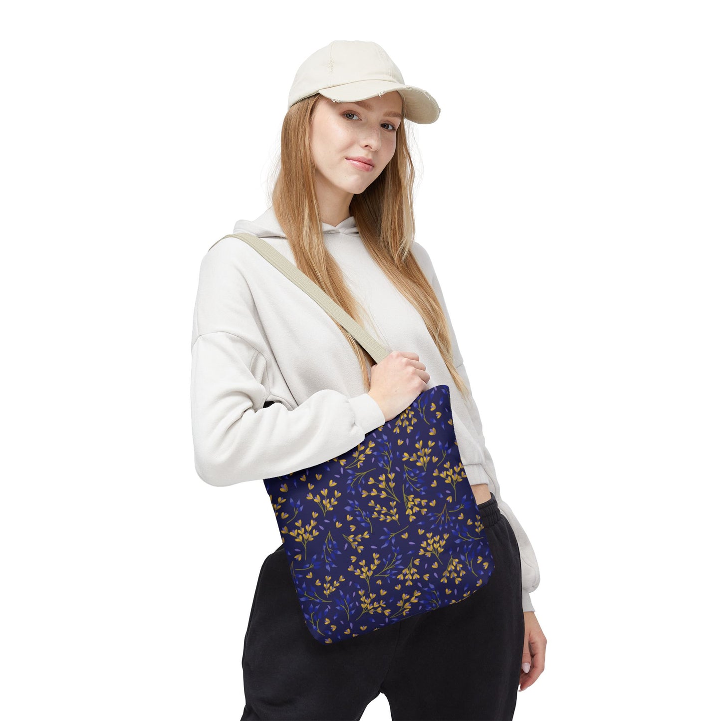 Young woman models the Floral Tote Bag, featuring a vibrant yellow and blue leafy sprig pattern. Perfect for summer outings, it complements her casual off-white hoodie and black pants ensemble.