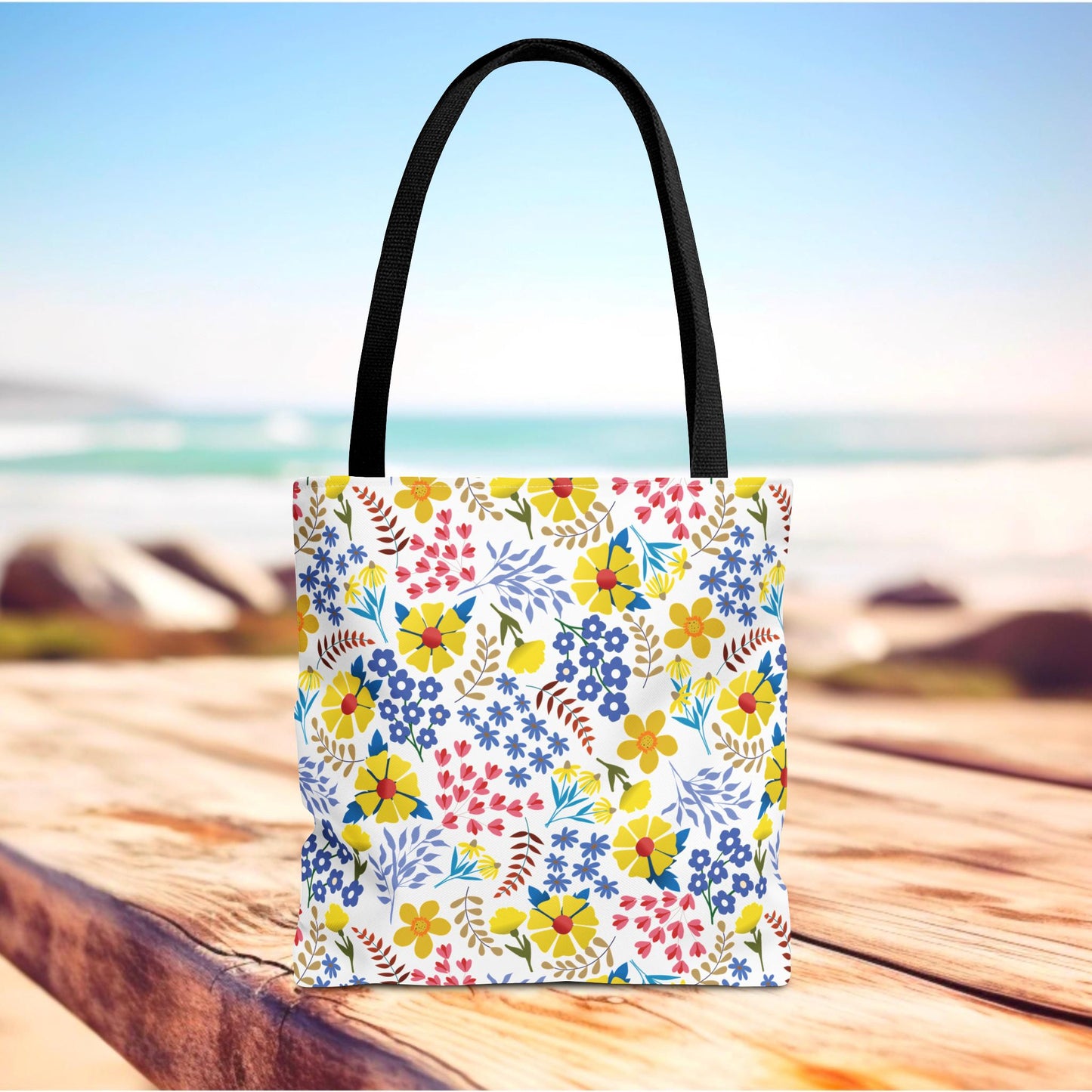 Floral Tote Bag with multicolor blooms and leafy sprigs on a white background, featuring black straps. Ideal for summer outings, this bag embodies FireBrook Essentials' joyful design ethos.