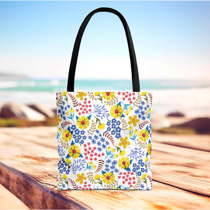Floral Tote Bag with multicolor blooms and leafy sprigs on a white background, featuring black straps. Ideal for summer outings, this bag embodies FireBrook Essentials' joyful design ethos.