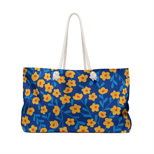 Weekender Bag with vibrant floral print on deep blue fabric, featuring thick white rope handles through metal eyelets. Spacious and stylish, ideal for travel, embodying FireBrook Designs' uplifting, practical style.