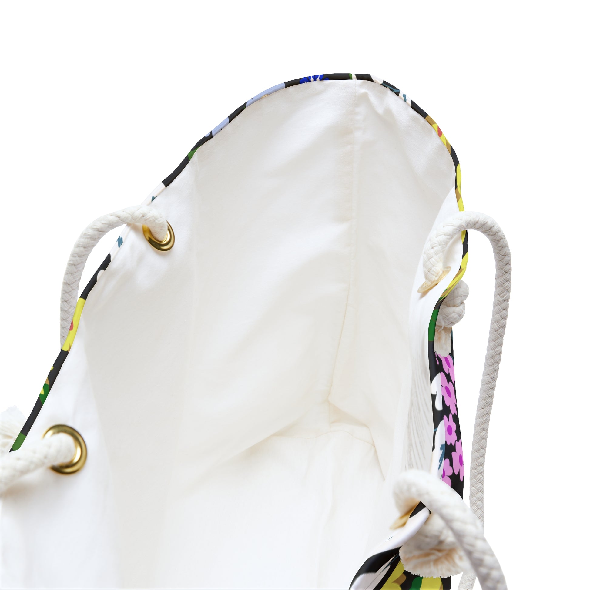 Weekender Bag with a cream-lined interior and braided rope handles through brass grommets, showcasing a hint of colorful floral print at the top edge, perfect for stylish travel.