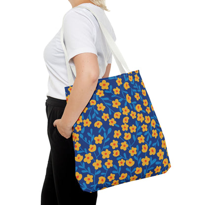 A person carries a Floral Tote Bag featuring a deep blue background with vibrant yellow-orange flowers and bright blue leaves, showcasing FireBrook Essentials' joyful and uplifting design.