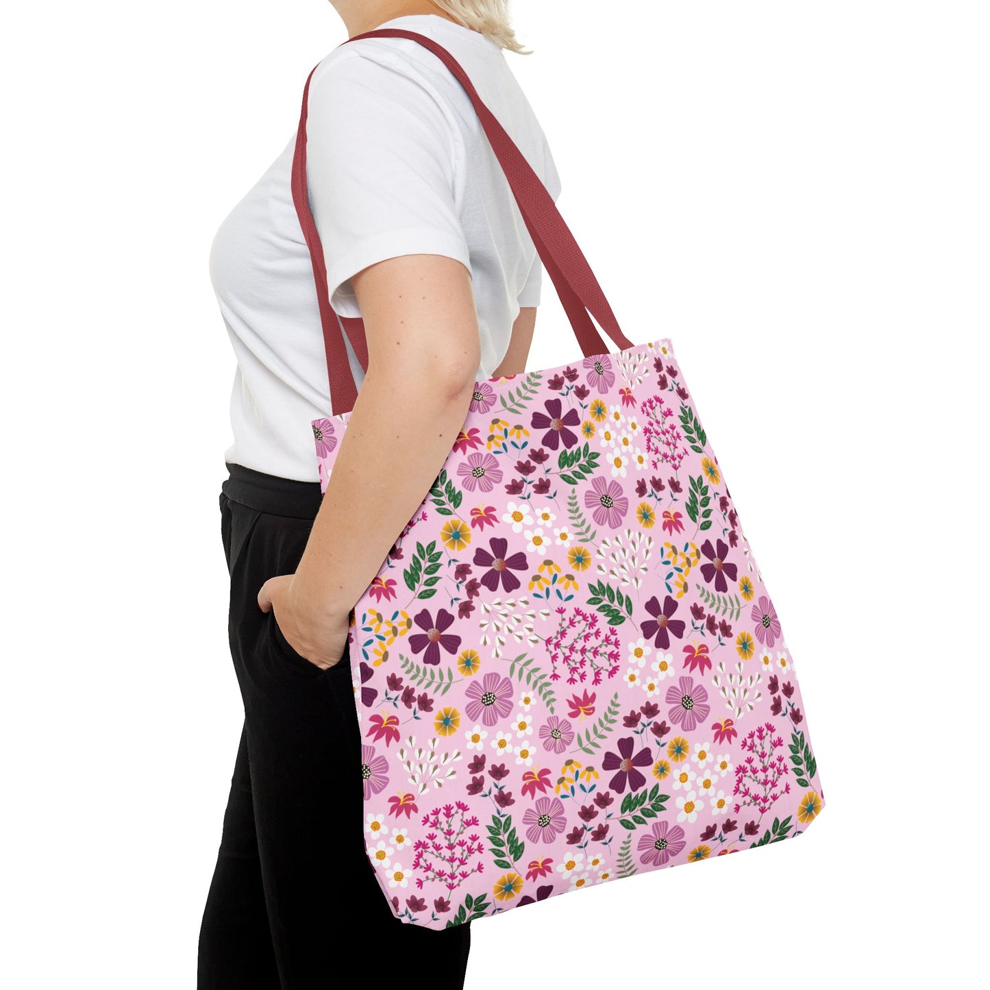 Person wearing a white T-shirt carries the Rose Garden Blush Tote Bag, featuring vibrant floral prints and burgundy straps, ideal for everyday essentials. The tote complements FireBrook Essentials' stylish, durable design ethos.