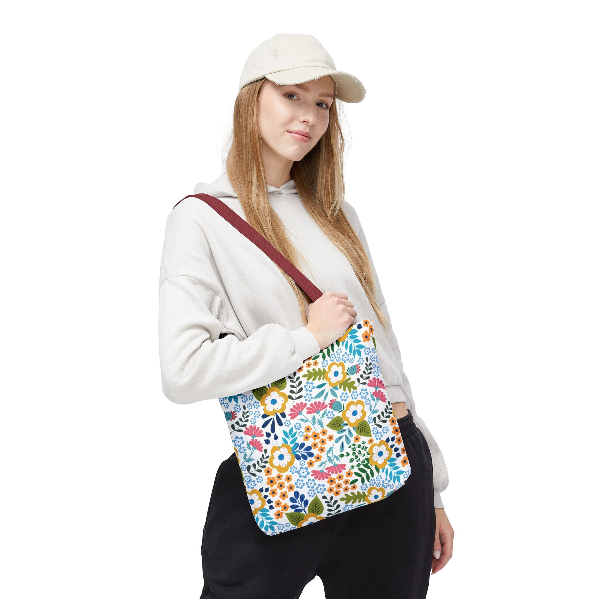 Person wearing light-colored hoodie and cream cap, carrying a Floral Tote Bag with multicolored floral print and burgundy strap, ideal for summer outings, showcasing FireBrook Designs’ uplifting, joyful style.