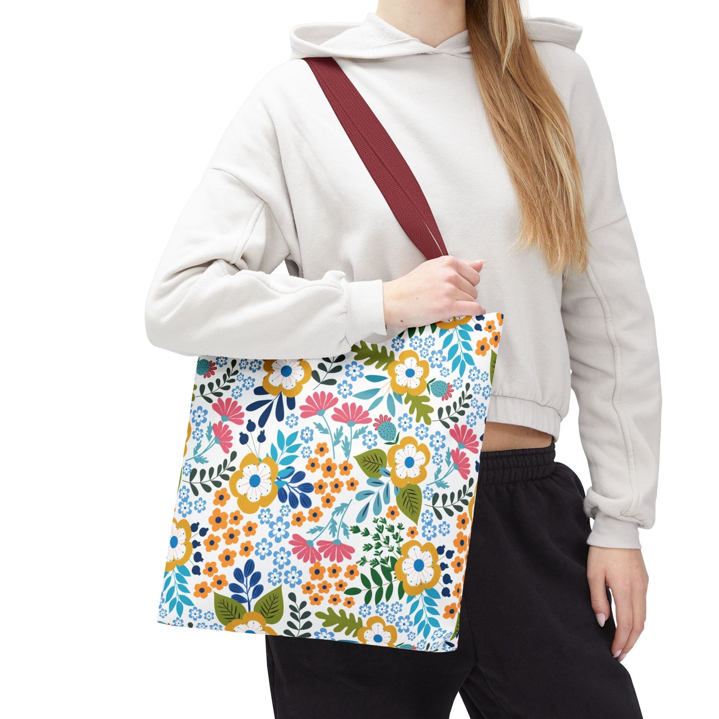 A person wearing a cropped hoodie carries a Floral Tote Bag over their shoulder. The tote features vibrant, stylized blooms with a burgundy-red strap, embodying FireBrook Designs' cheerful, uplifting aesthetic.