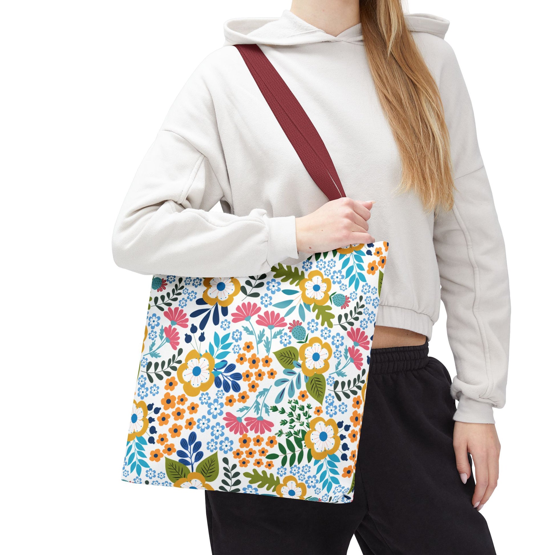 A person wearing a cropped hoodie carries a Floral Tote Bag over their shoulder. The tote features vibrant, stylized blooms with a burgundy-red strap, embodying FireBrook Designs' cheerful, uplifting aesthetic.
