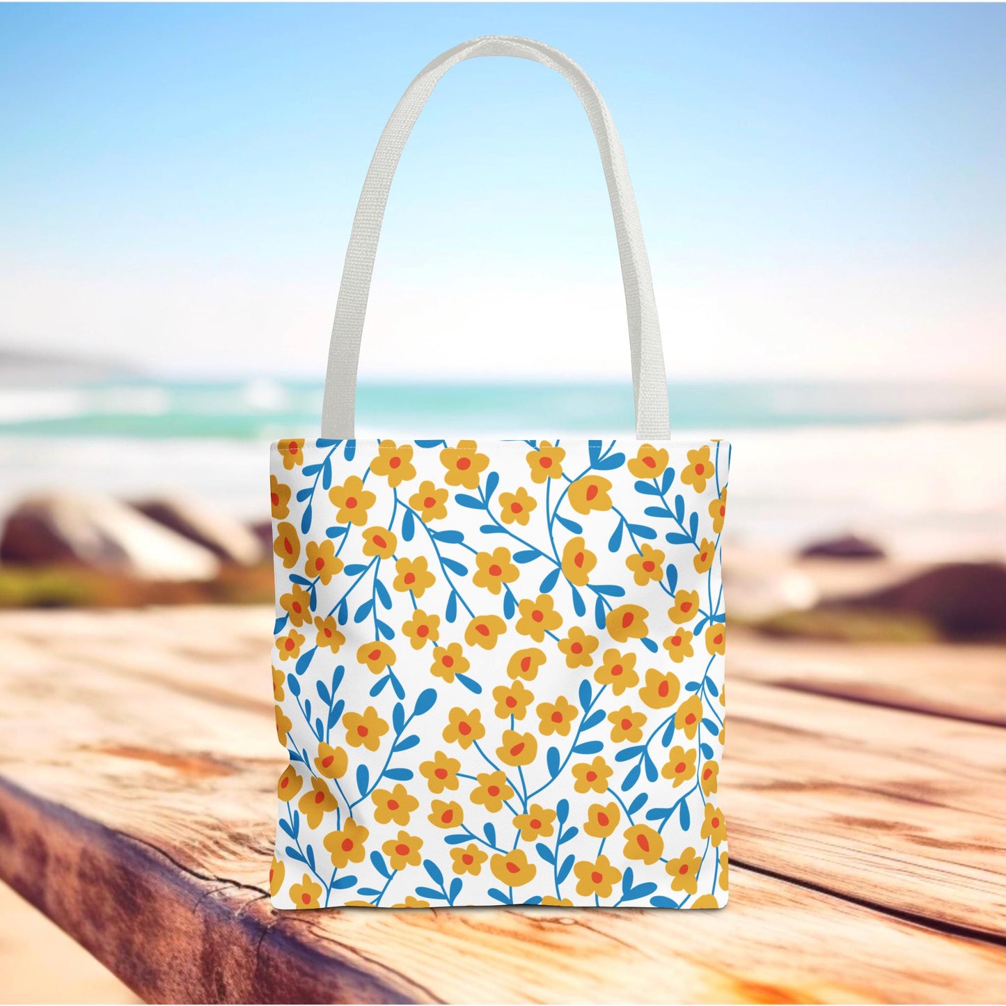 The Buttercup Cream Tote Bag features a vibrant pattern of yellow-orange flowers and blue foliage on a white background, perfect for summer. Its durable design suits beach trips or market visits.