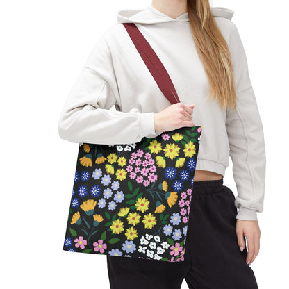 Starry Night Blooms Tote Bag is showcased over a person's shoulder, displaying its vibrant floral print on a black background with a burgundy-red strap, perfect for cheerful summer outings.
