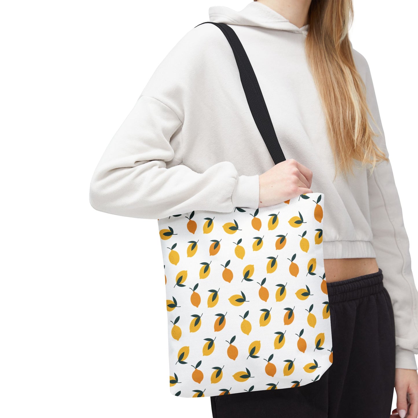 Lemon Drop Toss Tote Bag featuring vibrant citrus fruit pattern with green leaves on a white canvas, carried over the shoulder with a black strap, ideal for brightening everyday outings.