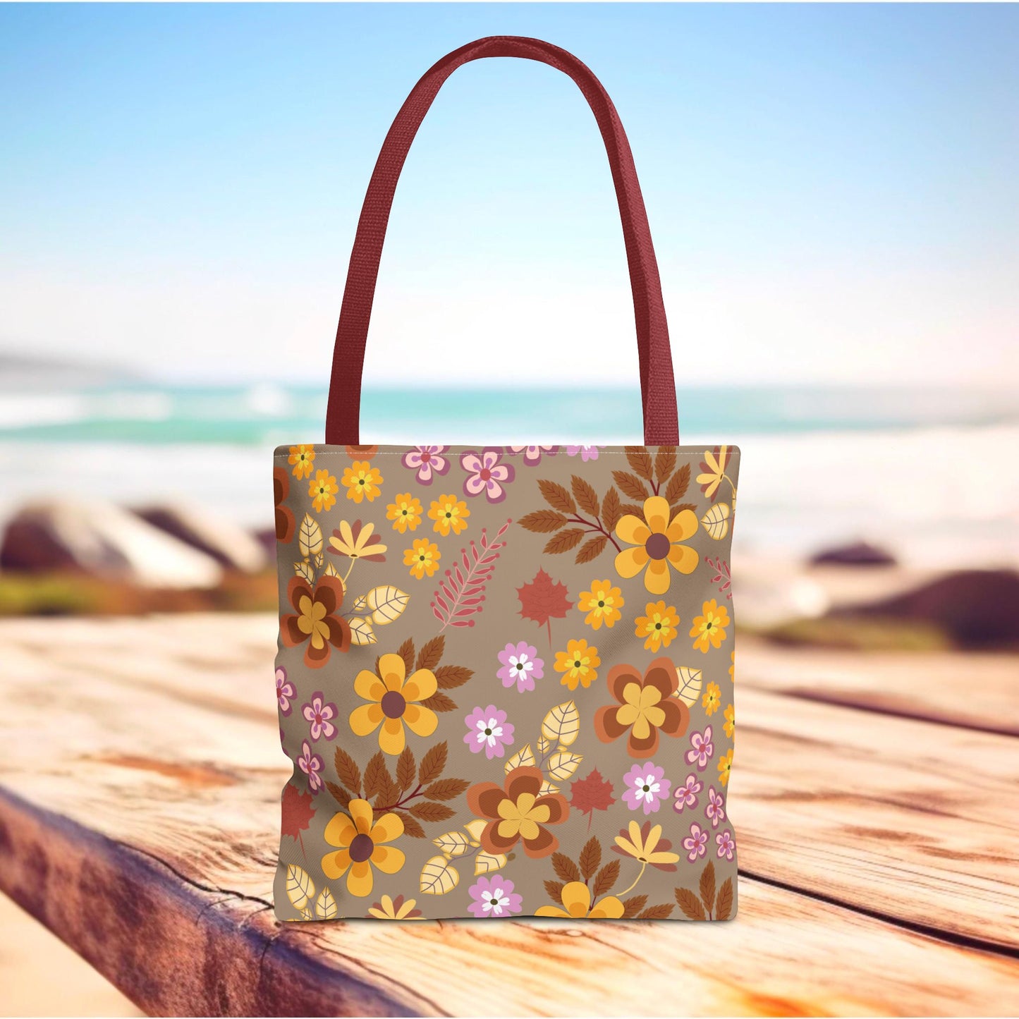 Harvest Brown Bloom Tote Bag with autumnal floral pattern on taupe, deep burgundy-red handles, set against a rustic wooden surface, ideal for joyful, stylish outings from FireBrook Designs.