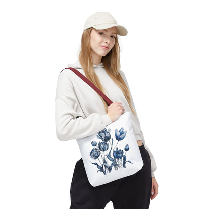 Woman wearing a hat and sweatshirt holds the Flowers in Blue Hue Watercolor Tote Bag, showcasing its floral design and sturdy construction.