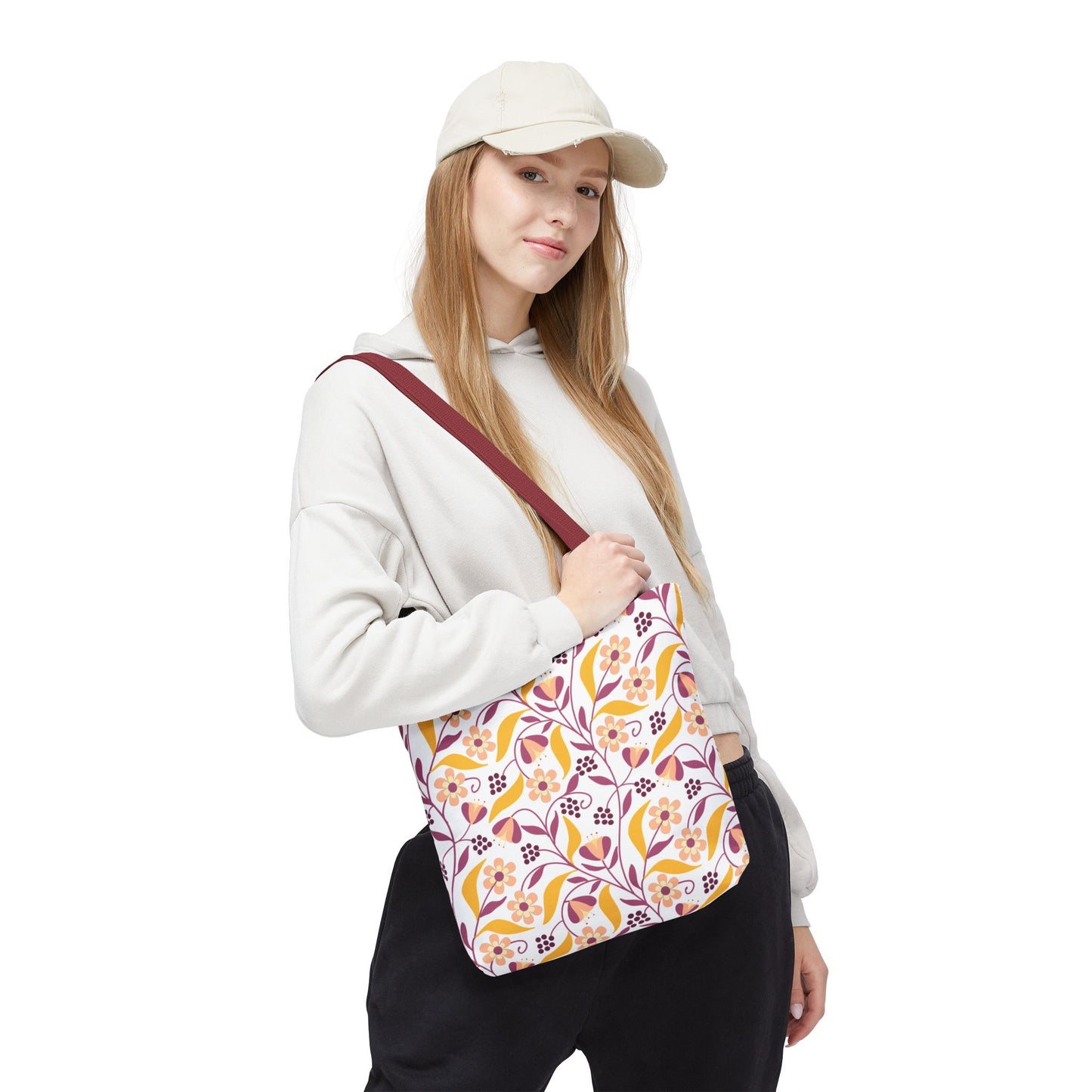 A young woman models the Floral Tote Bag, showcasing its vibrant floral-and-vine pattern in yellow, pink, and burgundy. Perfect for summer outings, it complements her casual hoodie and dark pants.
