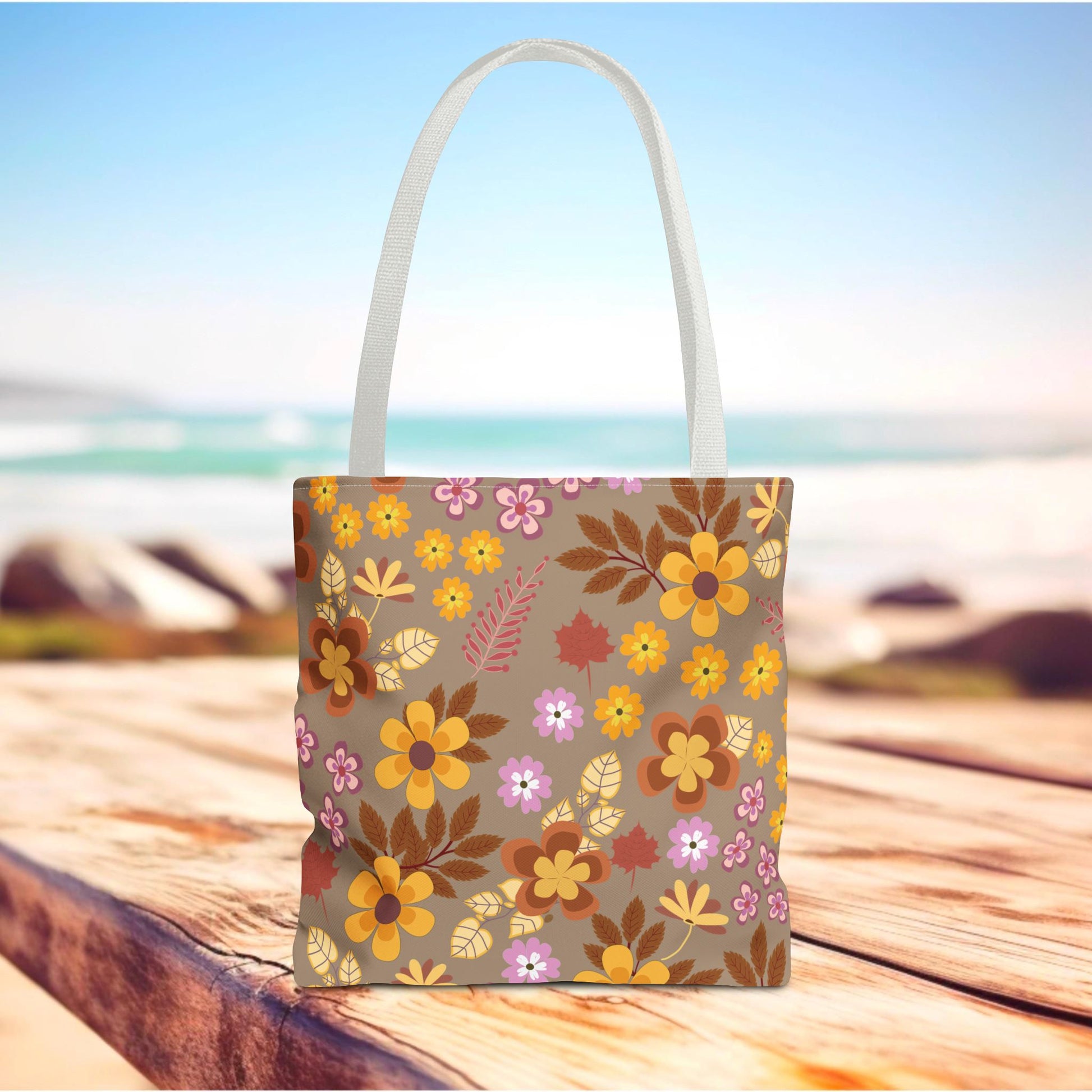 Harvest Brown Bloom Tote Bag featuring a vibrant fall-inspired floral pattern stands on a wooden boardwalk, perfect for joyful outings with its durable, quick-drying polyester build and reinforced white woven handles.