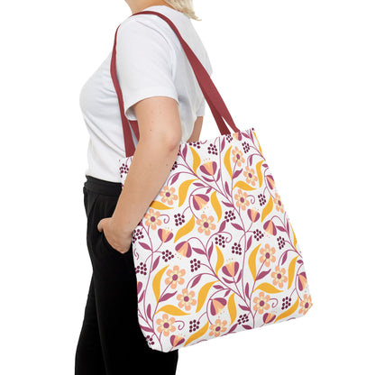 Floral Tote Bag with dark-red straps, featuring vibrant yellow, pink, and burgundy stylized flowers. Perfect for summer outings, carried over the shoulder by a person in casual attire. 