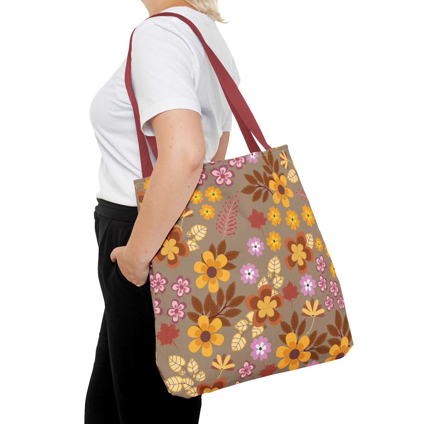 The Harvest Brown Bloom Tote Bag, featuring a vibrant retro floral pattern, is carried over a shoulder. Its burgundy straps and durable design make it ideal for joyful summer outings.