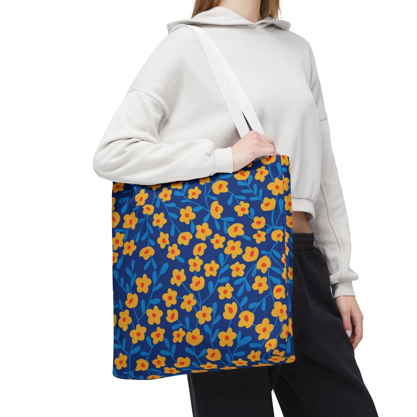 A person holds the Floral Tote Bag with a dark-blue background and cheerful yellow-orange flowers. Ideal for joyful summer outings, this durable tote embodies FireBrook Designs' uplifting style and practicality.