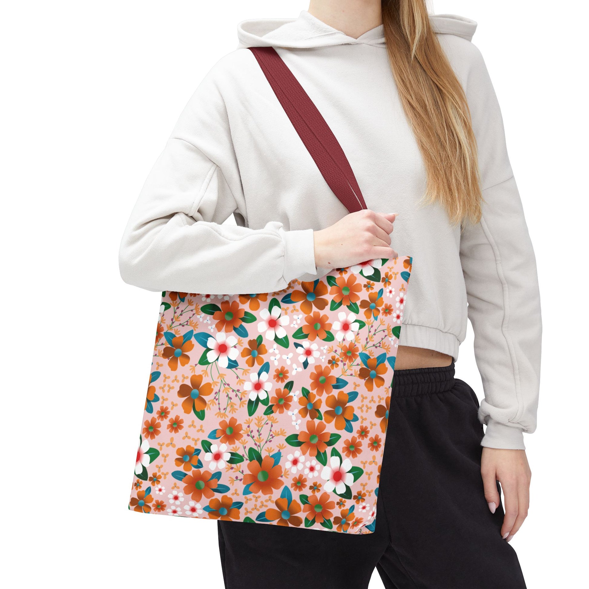 Floral Tote Bag over shoulder, featuring vibrant orange, white, and teal flowers on pink. Wide burgundy strap enhances style. Perfect for summer outings, aligning with FireBrook Essentials' uplifting, joyful design ethos.