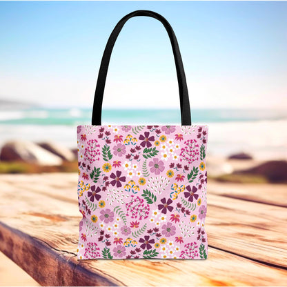 Floral Tote Bag with black straps, vibrant pink floral design, sits on wood surface. Durable and stylish, ideal for everyday use, reflecting FireBrook Essentials' commitment to joy and practicality.