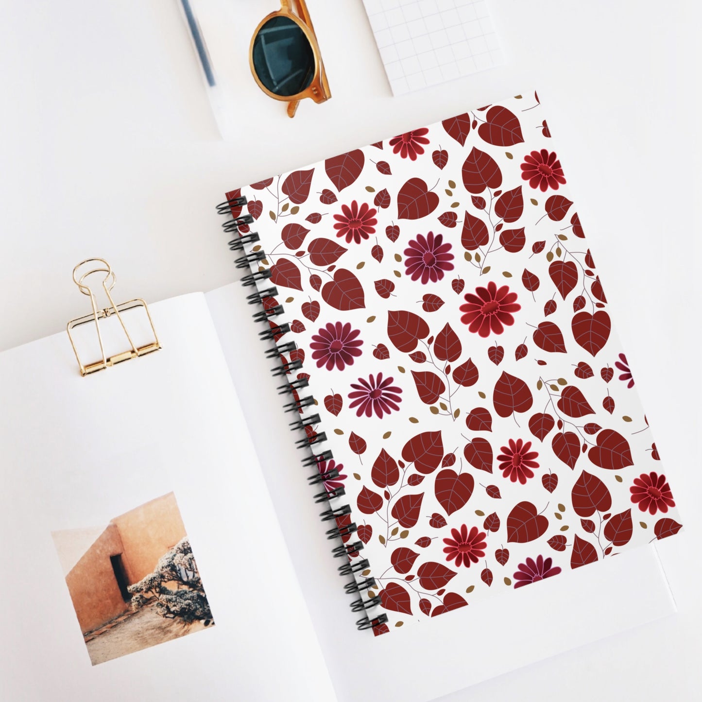 Spiral Notebook, Durable Cover, Ruled, 6x8 featuring a pattern of leaves and flowers, lies on a styled desktop with a magazine and round sunglasses, embodying FireBrook Essentials' blend of style and practicality.