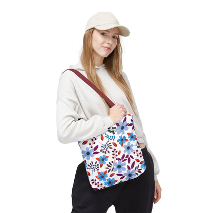 Floral Tote Bag held by a person wearing a light hoodie and cap, featuring a white base with blue, purple, and red blossoms, maroon strap, ideal for joyful summer outings.