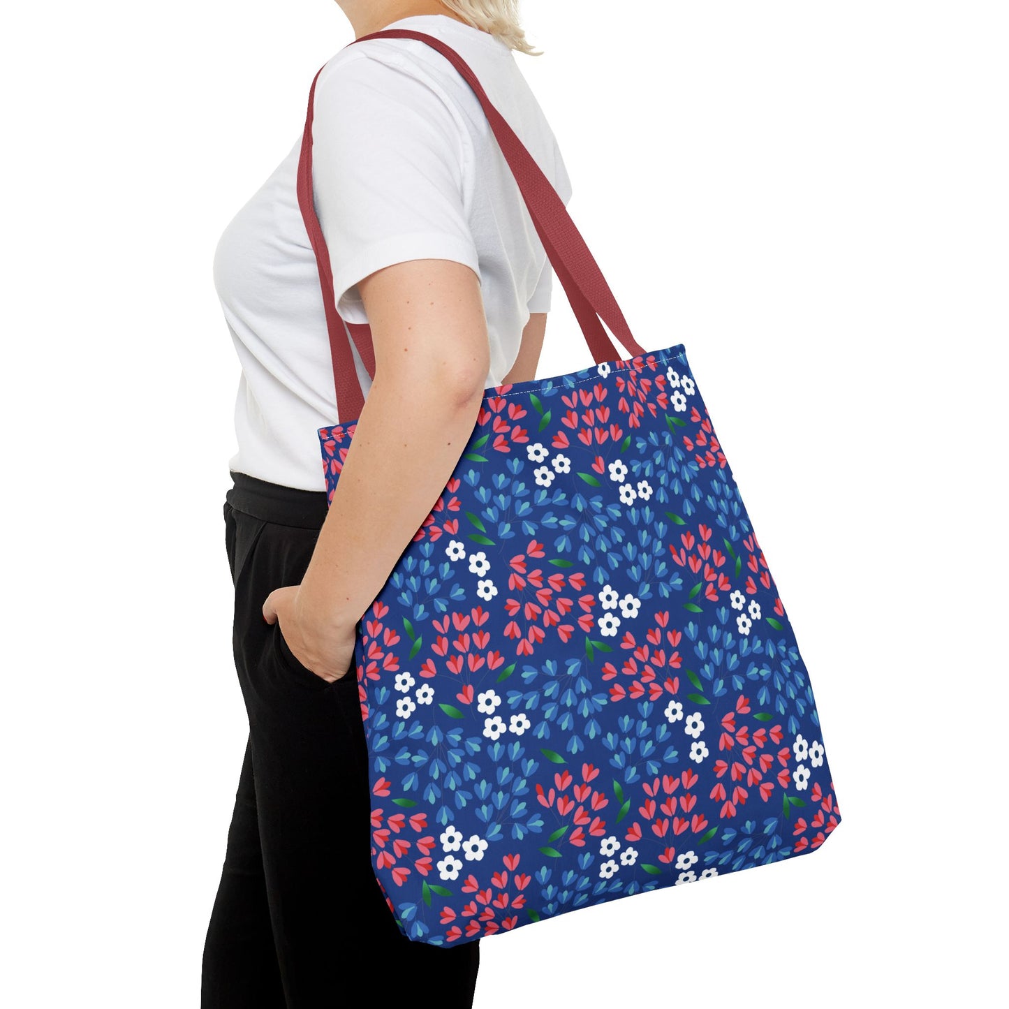 Person wearing a plain white T-shirt holds the Floral Tote Bag, featuring a navy blue body with a vibrant floral pattern and burgundy straps, ideal for cheerful, stylish summer outings.
